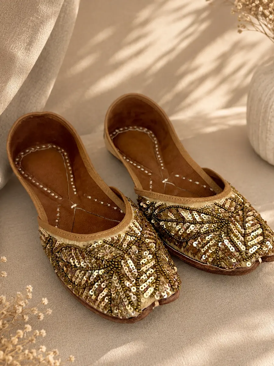 A pair of Gold Grace juttis resting on cream fabric, seen from an angle.