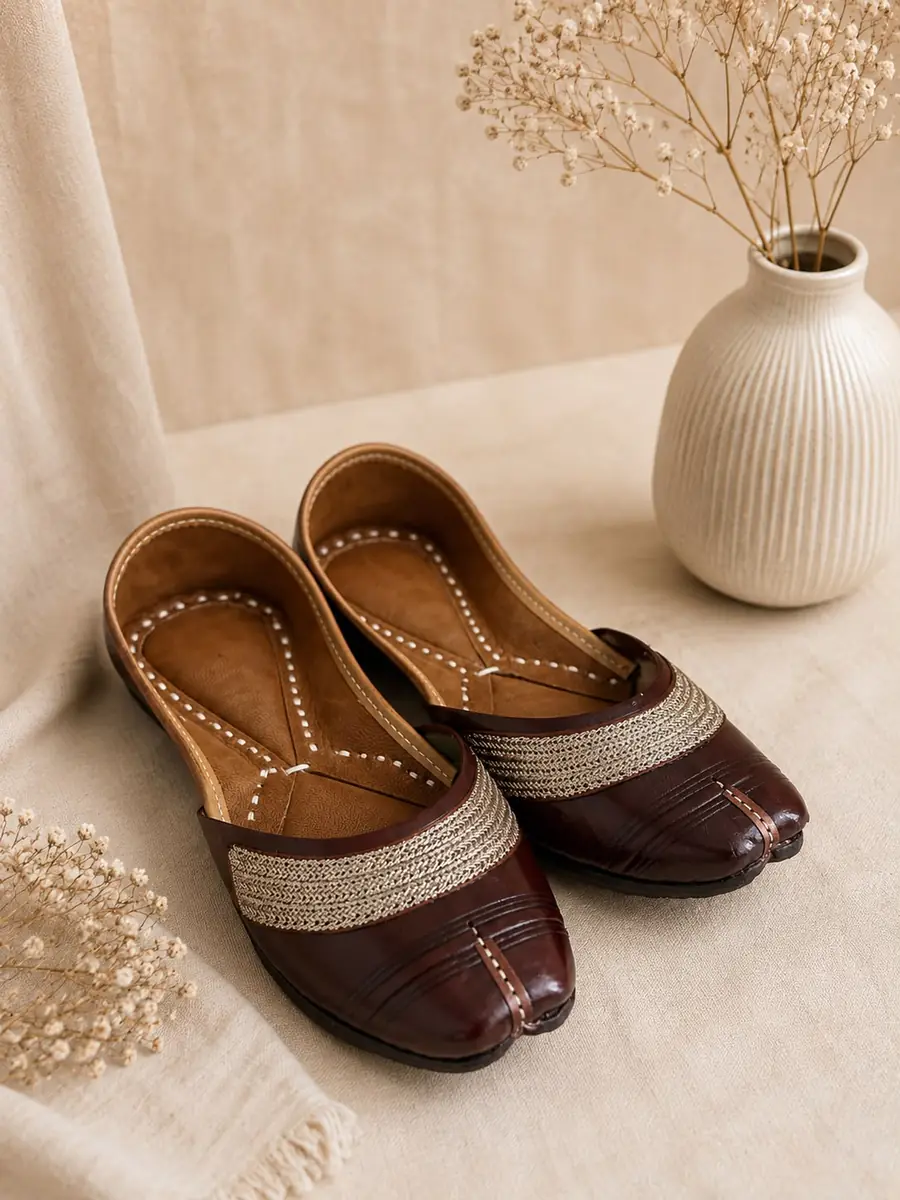 A pair of Mocha Grace juttis resting on cream fabric, seen from the side.