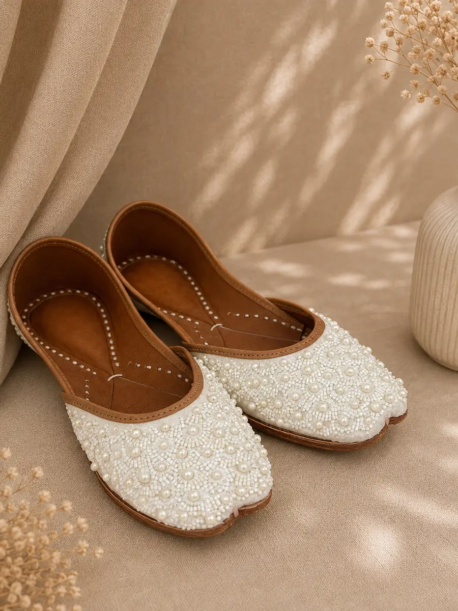 A pair of Pearl Grace juttis resting on cream fabric, seen from an angle.